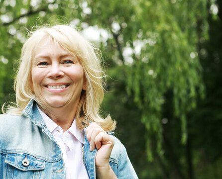 Beautiful blonde woman in a denim jacket in a spring park. Elderly happy lady pensioner. Close up.