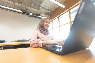 Asian Muslim woman wearing hijab working at office with documents on table, planning to analyze financial report, business plan, investing, financial concept and having fun at work