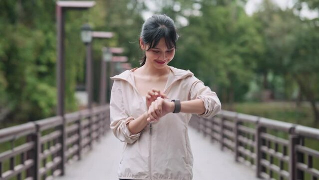 An Asian woman in workout attire is exercising with the smartwatch's fitness function in a public park. Capture the blend of technology and outdoor fitness for a vibrant image