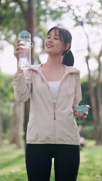 An Asian woman in workout attire is drinking water, taking a break from exercising in a public park. Showcase hydration and wellness during a fitness routine outdoors for a refreshing image