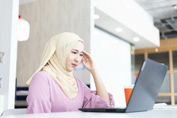 Asian Muslim woman wearing hijab working at office with documents on table, planning to analyze financial report, business plan, investing, financial concept and having fun at work