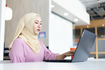 Asian Muslim woman wearing hijab working at office with documents on table, planning to analyze financial report, business plan, investing, financial concept and having fun at work