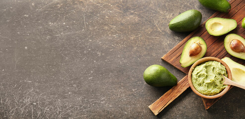 Wooden board with bowl of delicious guacamole and ripe avocados on dark grunge background with...