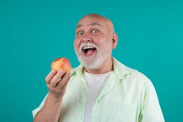 Funny Senior granddad eat apple in studio. Portrait of a elderly man eating an apple. Man biting...