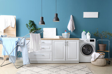 Laundry room interior with washing machine, white counters and clothes on drying rack
