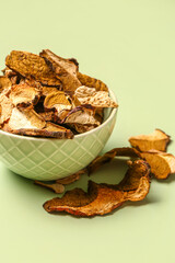 Bowl with tasty dried mushrooms on green background