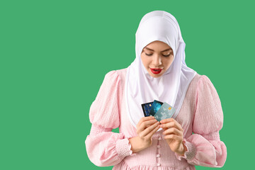 Beautiful Muslim woman with credit cards on green background