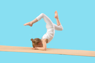 Cute little girl with mat doing gymnastics on blue background