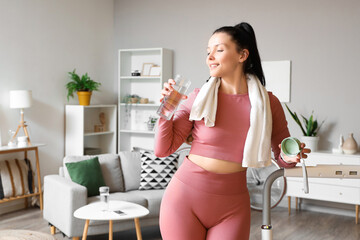 Sporty young woman with towel and water bottle at home - Powered by Adobe