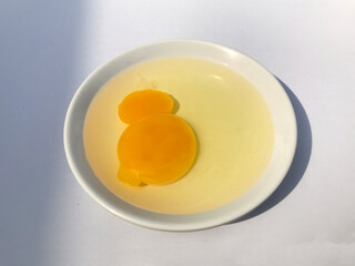 Broken chicken egg yolk on a white saucer on a white background.