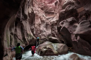  Extreme tourists walk along the Mujib River, flowing between high cliffs along the tourist route in the Mujib River canyon in Wadi al-Mujib in Jordan © svarshik
