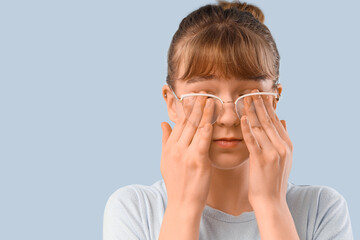 Young woman in glasses rubbing her eyes on light background, closeup. Glaucoma awareness month