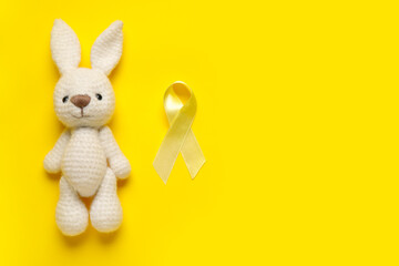 Golden ribbon with toy bunny on yellow background. Childhood cancer awareness concept