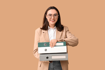 Young businesswoman with document folders on beige background