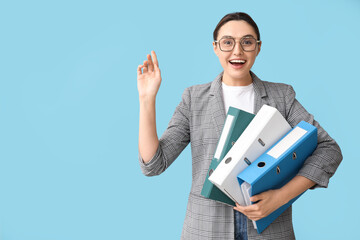Young businesswoman in eyeglasses with document folders on blue background