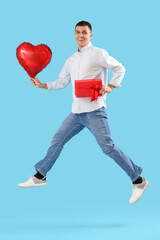 Young man with heart-shaped balloon and gift jumping on blue background. Valentine's Day celebration