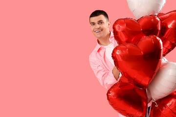 Young man with heart-shaped balloons on pink background. Valentine's Day celebration
