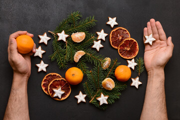 Male hands with star-shaped gingerbread cookies, mandarins, dried orange and fir branches on black background