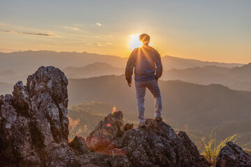 Young hiker male standing on top mountains cliff enjoying view of nature sunset