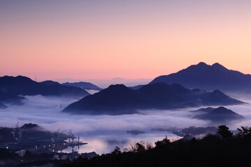 朝焼けに染まる海と雲海と造船所