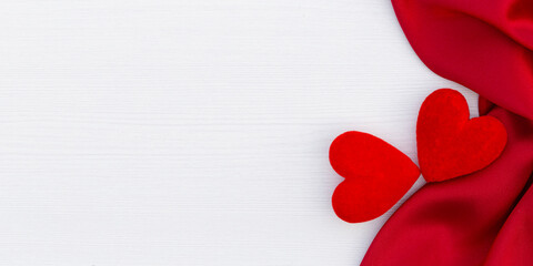 Red hearts and red satin on the white wooden background. Red ribbon. Valentine's Day gift.