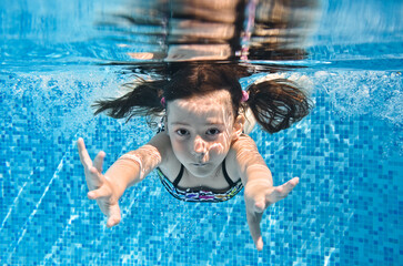 Child swims underwater in swimming pool, active little girl dives and has fun under water, kid...