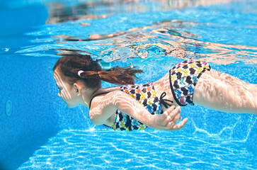Child swims underwater in swimming pool, active little girl dives and has fun under water, kid...