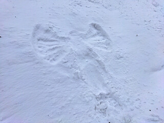 Snow angel made in a snowdrift in winter. View of a flat homemade sculpture on a white soft surface.