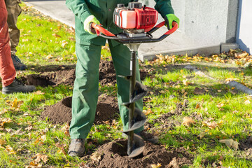 Gardener using tools hand-held soil hole drilling machine or portable manual earth auger.