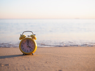 Yellow alarm clock on the beach in the sunset time. The concept about Time to summer, Travel,...