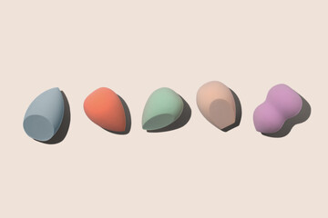 Set of colourful pastel blue, orange, biege, green and purple sponges for makeup on beige background with dark shadows. Beauty blender with different shape. 