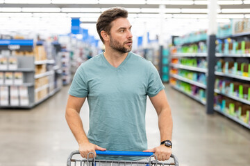 Handsome man with shopping basket with shopping trolley at grocery. Man buying groceries in supermarket. Male model in shop. Concept of shopping at supermarket.