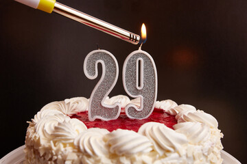 A candle in the form of the number 29, stuck in a festive cake, is lit. Celebrating a birthday or a...