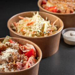 Salads in a paper take-out container with sauce on a black background. Healthy eating concept, food...