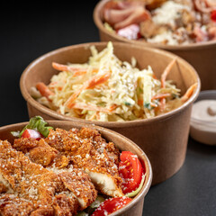 Salads in a paper take-out container with sauce on a black background. Healthy eating concept, food delivery to restaurant.