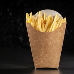 French fries in a paper basket. Fast food.French fries in a paper box on black background, menu food concept.