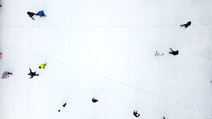 Many people skating on white ice skating rink outdoors on winter day top view. Aerial drone view. New Year Christmas celebration holidays recreation sport enjoying lifestyle sportive fun background. - obrazy, fototapety, plakaty