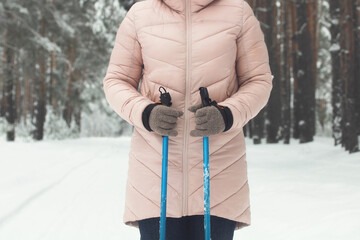 Nordic walking sticks in women's hands. a girl in a pink down jacket on a walk in the winter forest.