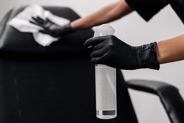 A woman wearing black medical gloves wipes the patient's receiving area with an antibacterial...
