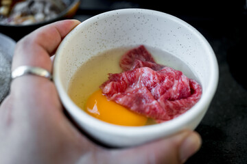 Man holding a white bowl premium fresh beef put in raw yolk egg for boiled Japanese Sukiyaki