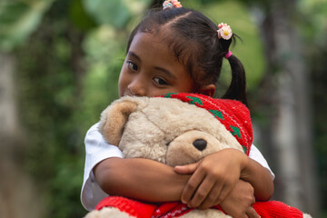 A cute young Filipino girl holding a large teddy bear wearing a Christmas Outfit. Embracing her favorite toy.