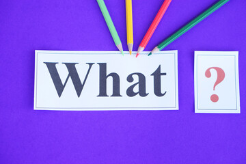 Paper cards with text  What and question marks. color pencils on purple background. Concept. Teaching aid. Education materials for teach WH- question. Asking questions.Suspicious symbol to find answer