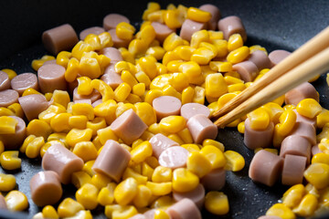 魚肉ソーセージと粒コーンを炒める調理シーン。
