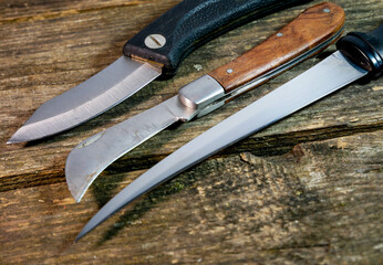 Three different knives on aged weathered pine wood boards.