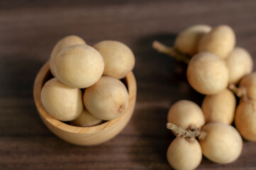 Langsat, Longkong, placed in a wooden cup set on a wooden board table dark blurred background