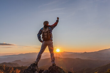 Success hiker male raised hand with backpack enjoy sunset at the top of a rock mountain.