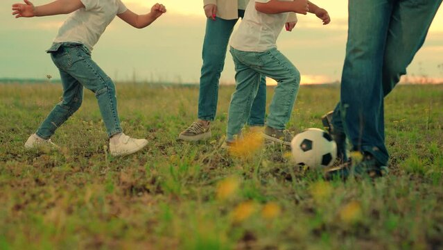 Family have fun playing soccer ball on lawn in park. Young family sport soccer team playing outdoors. Happy family playing football. Child kicks ball. Mom dad child play together, teamwork. Weekend