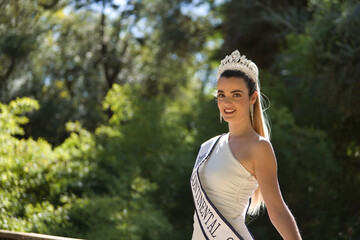 Portrait of young, beautiful, blonde woman in white suit, diamond crown and beauty pageant winner's...