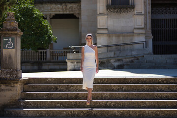 Young, pretty, blonde woman in a white suit and heels, walking down a staircase, self-confident and...