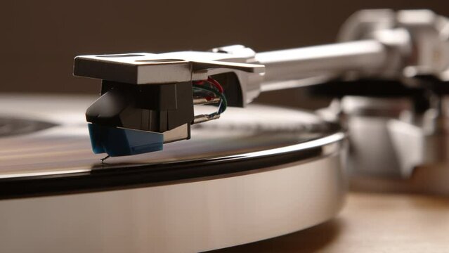 A close up macro shot highlighting the detailed interaction of a turntable's needle and stylus with the grooves of a vinyl record, set against the blurred backdrop of the tonearm and cartridge.